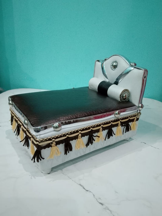 Silver Bed for Laddu Gopal Radha Krishna with black leather top and tassels on a white surface with teal background