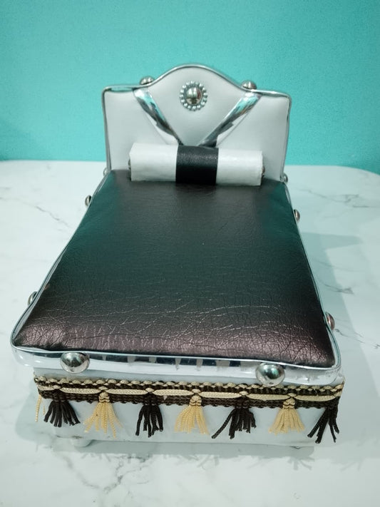 Silver Bed for Laddu Gopal Radha Krishna with black leather top and tassels on a white surface with teal background