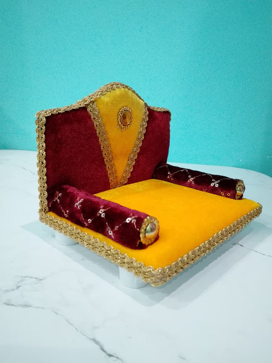 Singhasan for Gopal ji with red and yellow cushions on a white surface with teal background