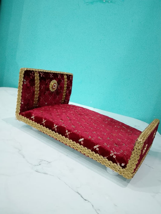 Red velvet bed with gold trim on a white surface against a teal background for Laddu gopal and Radha Krishna