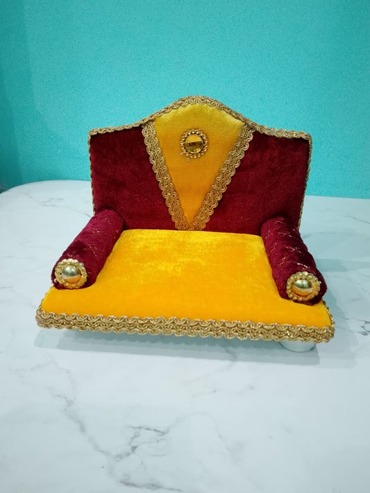 Singhasan for Gopal ji with red and yellow cushions on a white surface with teal background