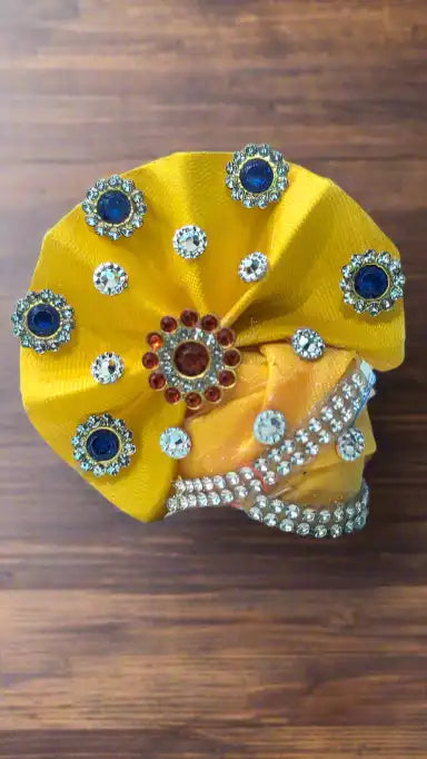 Yellow Laddu Gopal pagdi fabric item with decorative stones on a wooden surface